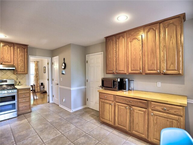 kitchen with brown cabinets, appliances with stainless steel finishes, backsplash, baseboards, and under cabinet range hood