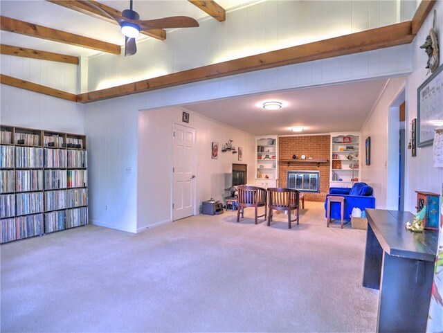 interior space featuring a brick fireplace, ceiling fan, beamed ceiling, and carpet