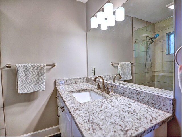 bathroom with vanity, baseboards, tiled shower, and a chandelier