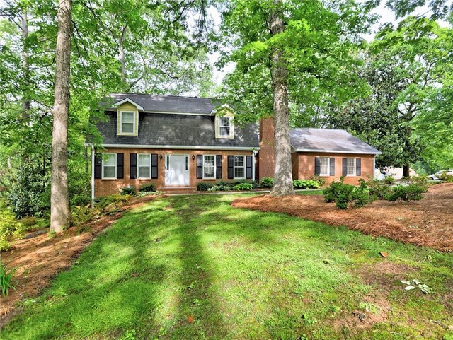 dutch colonial with brick siding, roof with shingles, and a front yard