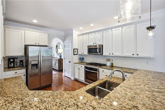 kitchen featuring a sink, light stone counters, crown molding, arched walkways, and appliances with stainless steel finishes