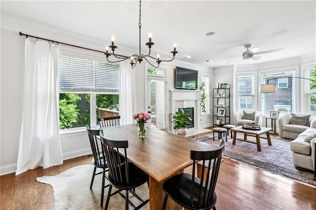 dining area with wood finished floors, ceiling fan with notable chandelier, crown molding, baseboards, and a high end fireplace