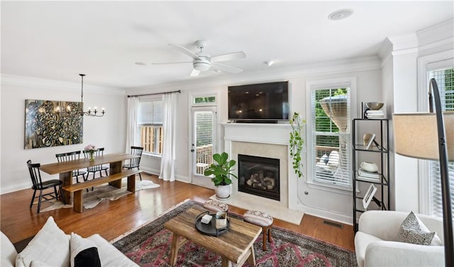 living area featuring ceiling fan with notable chandelier, a high end fireplace, wood finished floors, crown molding, and baseboards