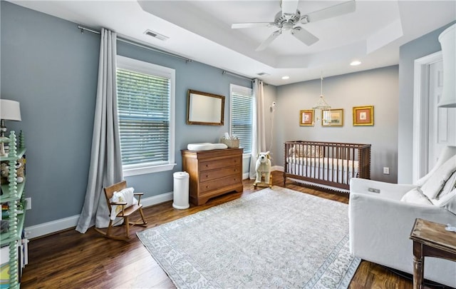 bedroom featuring a tray ceiling, baseboards, visible vents, and wood finished floors
