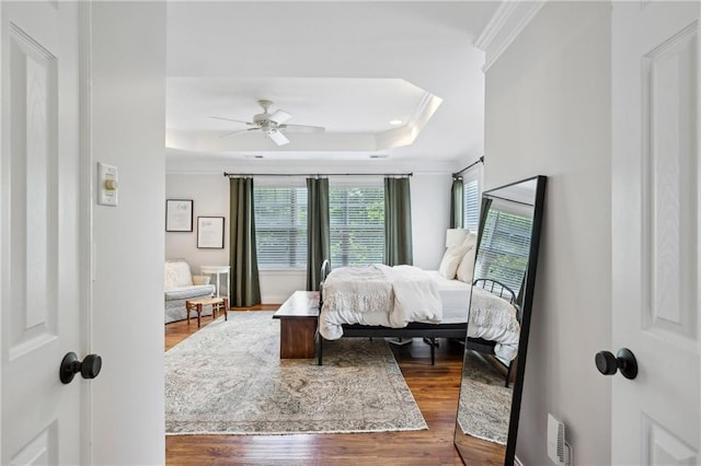bedroom featuring a ceiling fan, visible vents, crown molding, wood finished floors, and a raised ceiling