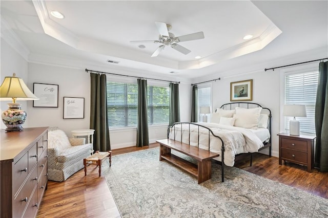 bedroom featuring a tray ceiling, multiple windows, visible vents, and wood finished floors