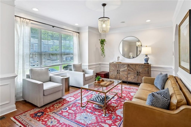 living area with wood finished floors, a wainscoted wall, crown molding, visible vents, and a decorative wall