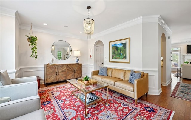 living room featuring ornamental molding, arched walkways, a wainscoted wall, and wood finished floors