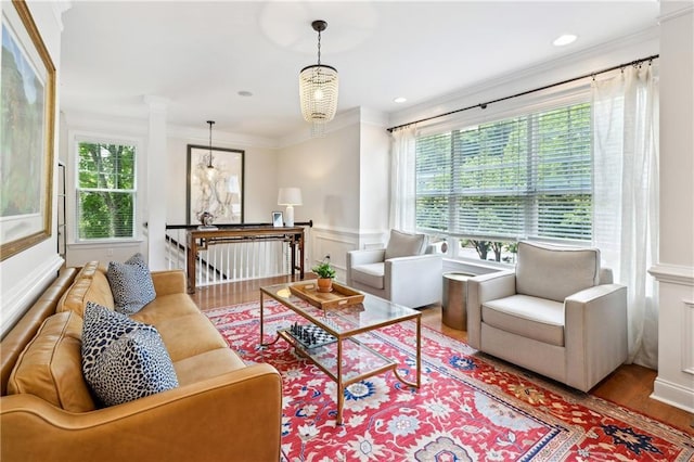 living area with wood finished floors, decorative columns, a decorative wall, wainscoting, and ornamental molding