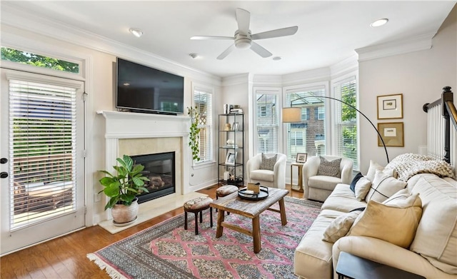 living room featuring wood finished floors, baseboards, ceiling fan, ornamental molding, and a high end fireplace
