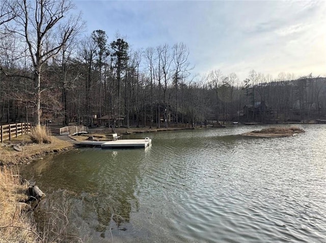 property view of water with a floating dock, a view of trees, and fence