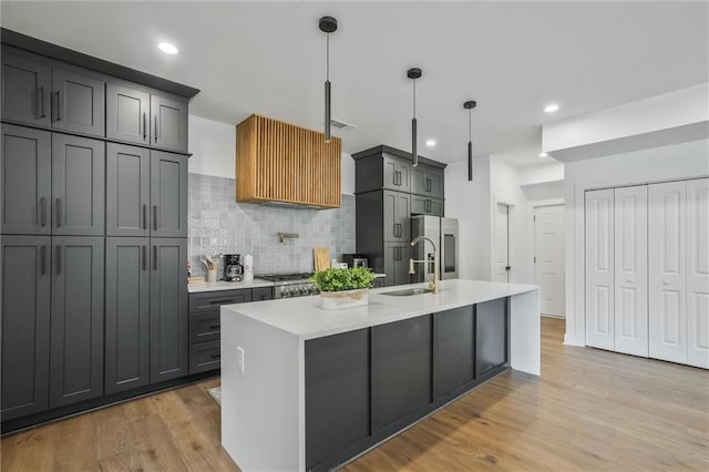2809 Glenwood Ave SE, Atlanta, GA 30317 - kitchen with decorative backsplash, light countertops, light wood-style floors, an island with sink, and stainless steel fridge