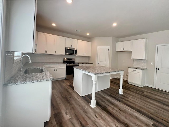 kitchen with light stone countertops, appliances with stainless steel finishes, sink, a center island, and white cabinetry