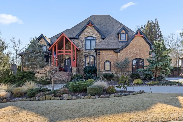 view of front of property featuring brick siding, a shingled roof, stone siding, french doors, and a front yard