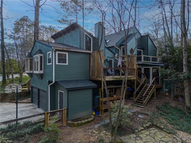 rear view of property featuring a chimney, a shingled roof, a garage, driveway, and stairs