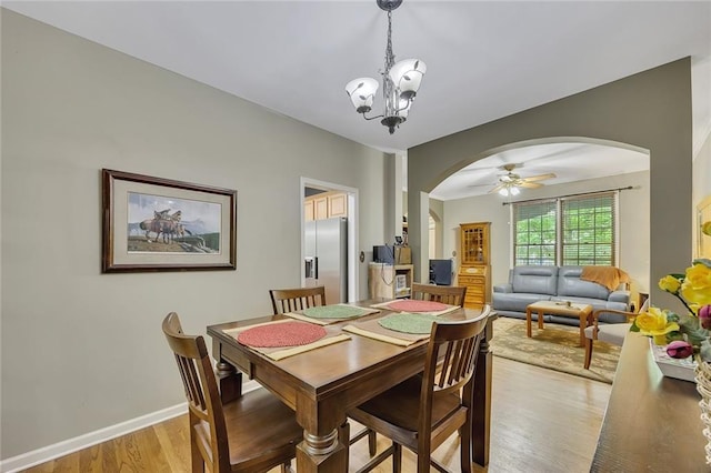 dining room featuring arched walkways, baseboards, ceiling fan with notable chandelier, and light wood-style flooring