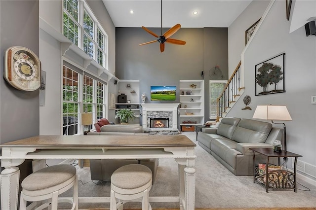 living room featuring ceiling fan, a stone fireplace, recessed lighting, baseboards, and a towering ceiling
