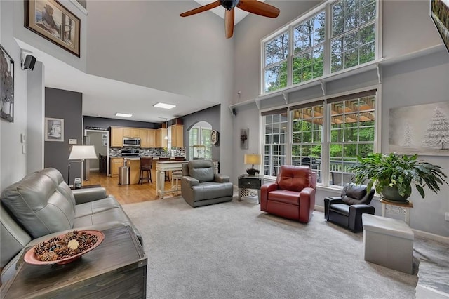 living area with baseboards, ceiling fan, light colored carpet, and a towering ceiling