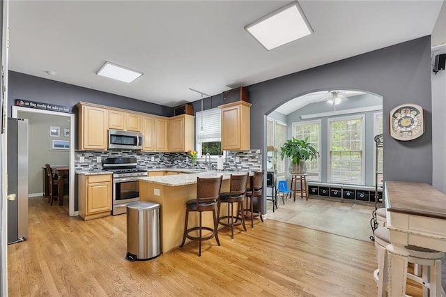 kitchen with light brown cabinetry, arched walkways, stainless steel appliances, a peninsula, and backsplash