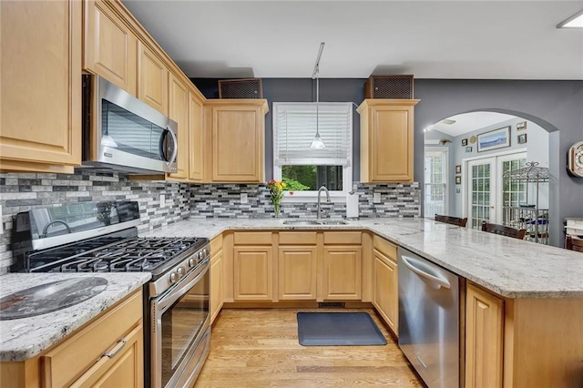 kitchen with a peninsula, light brown cabinets, arched walkways, a sink, and stainless steel appliances