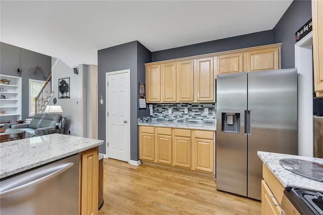 kitchen featuring light brown cabinetry, light wood-type flooring, light stone counters, appliances with stainless steel finishes, and backsplash