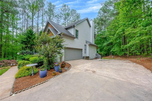 view of side of property featuring driveway, a chimney, and a garage