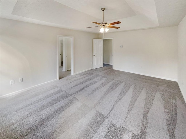 unfurnished room featuring a tray ceiling, baseboards, carpet floors, and ceiling fan