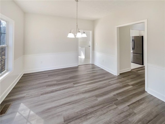 unfurnished dining area with visible vents, baseboards, an inviting chandelier, and wood finished floors