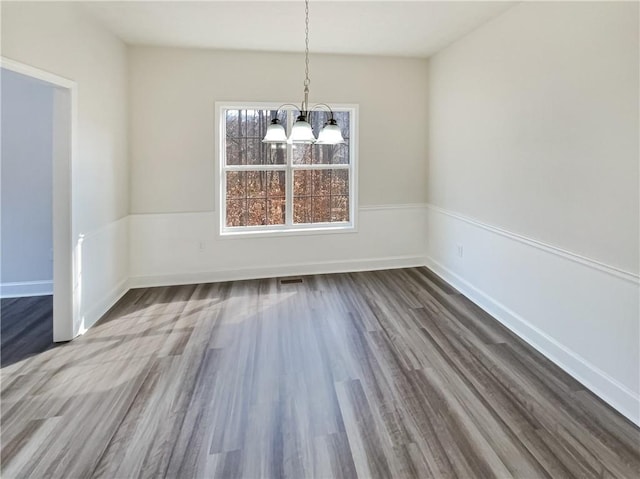 unfurnished dining area featuring a notable chandelier, visible vents, baseboards, and wood finished floors