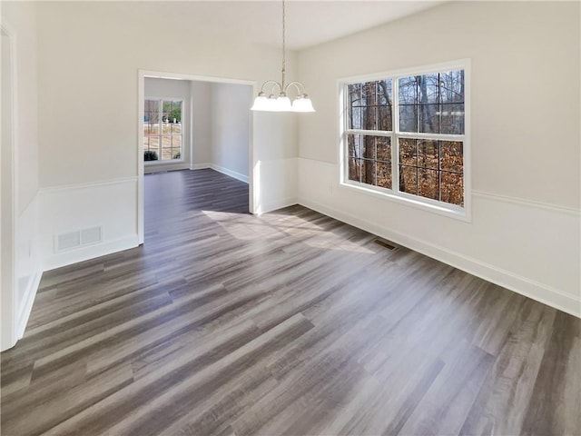 unfurnished dining area featuring visible vents, baseboards, an inviting chandelier, and dark wood-style flooring