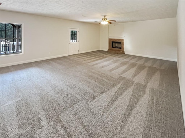 unfurnished living room with a textured ceiling, carpet, baseboards, ceiling fan, and a tile fireplace