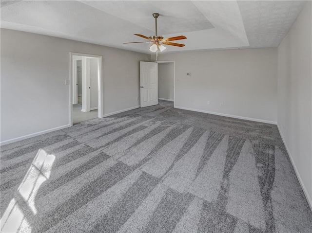 unfurnished room featuring a tray ceiling, baseboards, carpet, and a ceiling fan