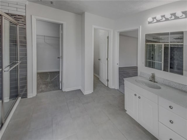 full bath with a walk in closet, baseboards, a textured ceiling, and vanity