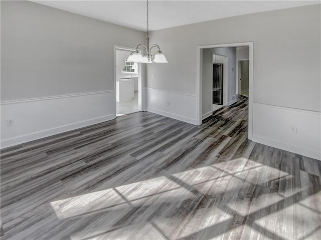 empty room with a chandelier, baseboards, and wood finished floors