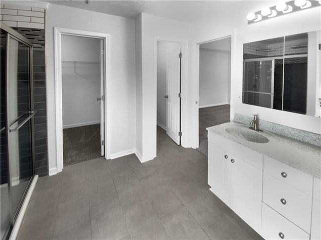 bathroom with a walk in closet, an enclosed shower, vanity, and baseboards