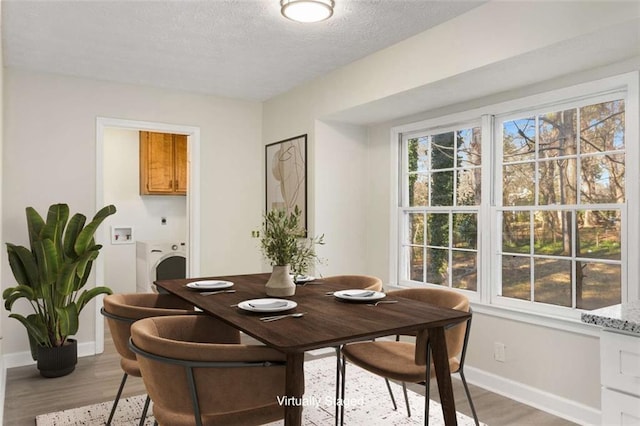 dining space with light wood finished floors, baseboards, washer / clothes dryer, and a wealth of natural light