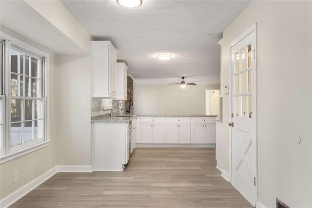 kitchen featuring baseboards, light wood-style flooring, a textured ceiling, white cabinetry, and a sink