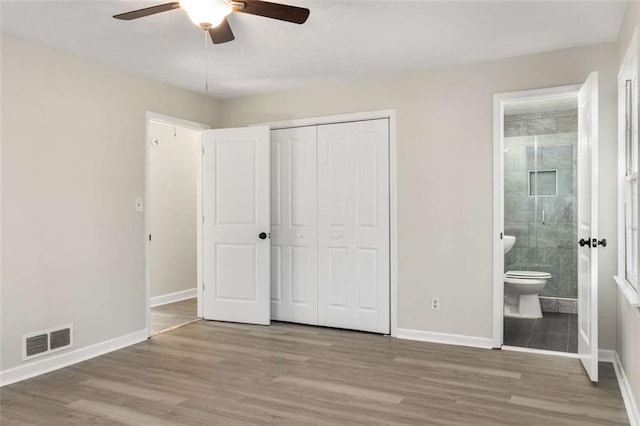 unfurnished bedroom with a closet, wood finished floors, visible vents, and baseboards