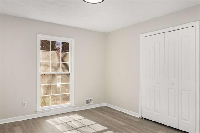 unfurnished bedroom featuring visible vents, baseboards, a closet, and wood finished floors