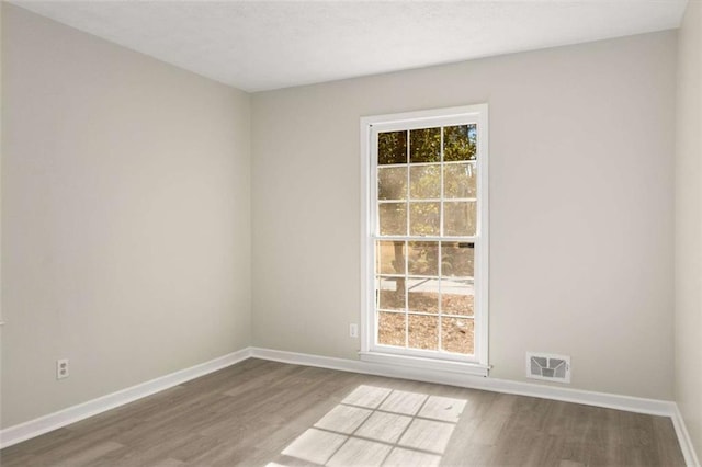 empty room with wood finished floors, visible vents, and baseboards