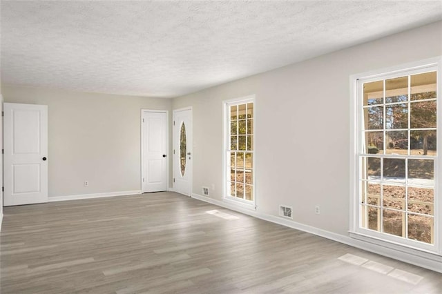 unfurnished room with plenty of natural light, wood finished floors, visible vents, and baseboards