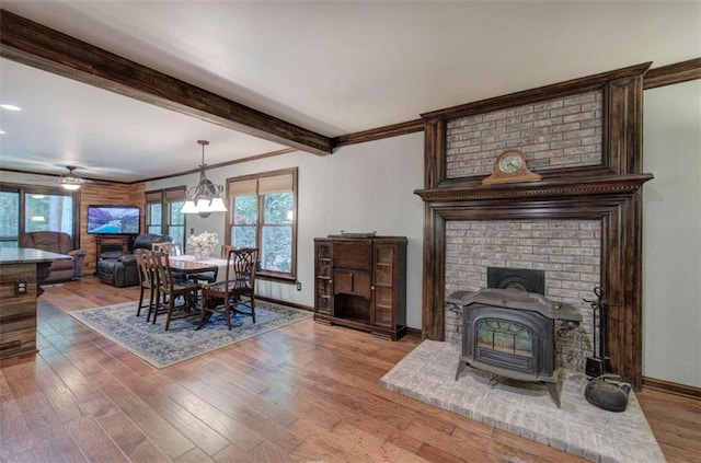 dining room featuring ceiling fan, wood-type flooring, crown molding, beamed ceiling, and a wood stove