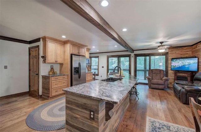 kitchen with sink, light hardwood / wood-style floors, beamed ceiling, stainless steel fridge with ice dispenser, and a kitchen island with sink