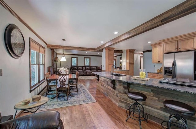 kitchen with hanging light fixtures, stainless steel fridge with ice dispenser, light hardwood / wood-style flooring, dark stone countertops, and sink