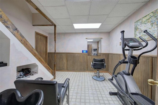 workout room with a paneled ceiling and wood walls