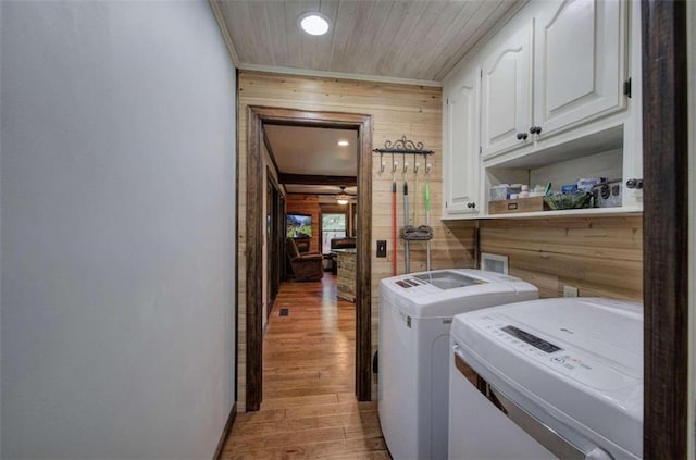 laundry room with washer and dryer, cabinets, light wood-type flooring, and wooden walls