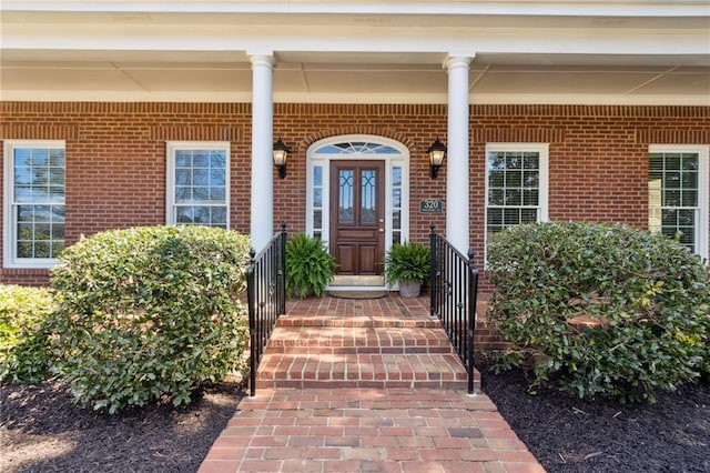 view of exterior entry featuring brick siding and covered porch