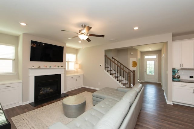 living area with dark wood finished floors, stairway, a ceiling fan, and baseboards