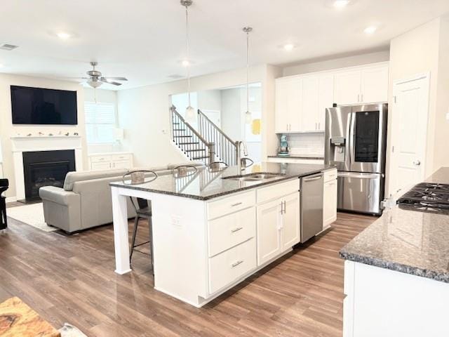 kitchen featuring a sink, dark stone counters, wood finished floors, ceiling fan, and appliances with stainless steel finishes