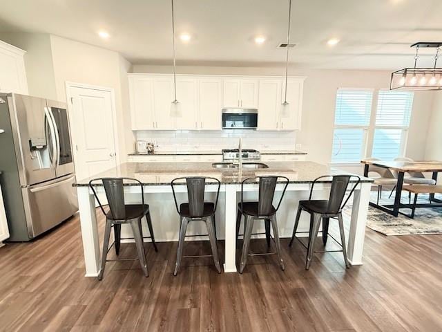 kitchen featuring an island with sink, backsplash, dark wood-style flooring, appliances with stainless steel finishes, and white cabinetry